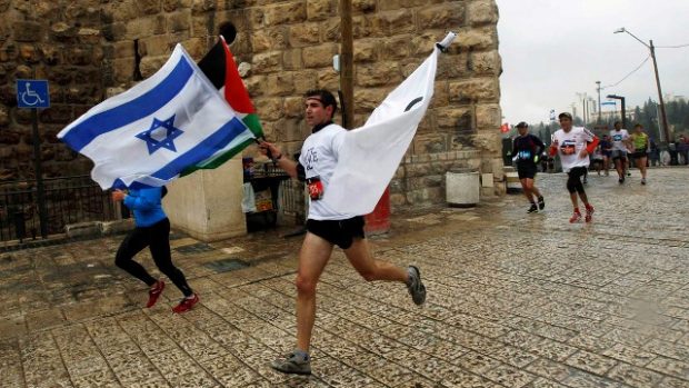 Běžec s iraelskou a palestinskou vlajkou na trati maratonu v Jeruzalémě