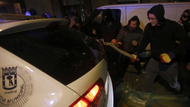 Demonstranti rozbíjejí zadní sklo auta místní policie v průběhu střetů s policií při protestech proti novému bezpešnostnímu zákonu