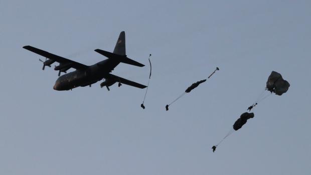 Parašutisté vyskakují z amerického dopravního letadla C-130 Herkules.