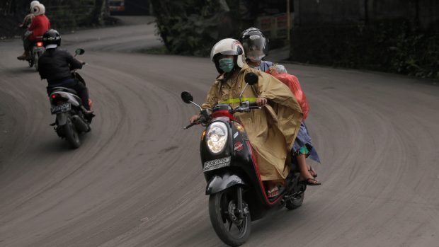 Lidé na Bali jedou na skútrech po cestě pokryté popelem ze sopky Agung