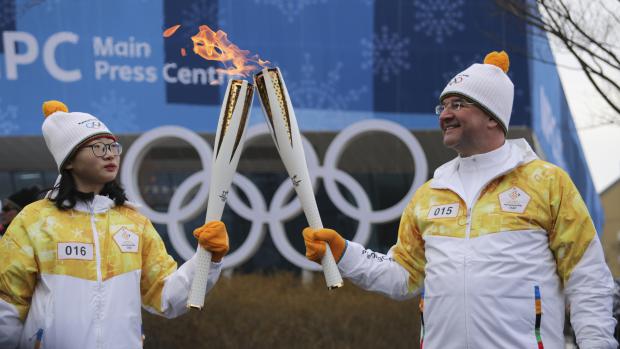 Dobrovolníci si předávají olympijský oheň