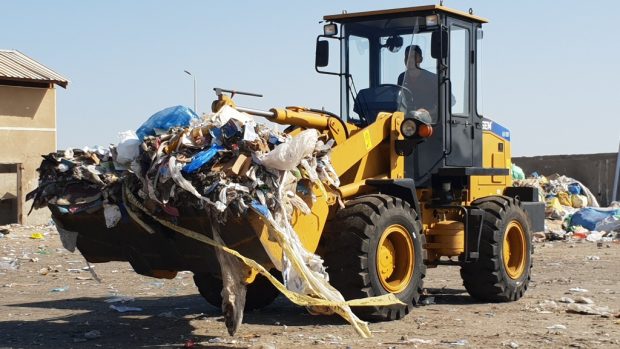 V betonové ohradě, v poušti kousek za Hurghádou, vysypává nakladač lžíci plnou pytlů s odpadky do úst recyklační linky.