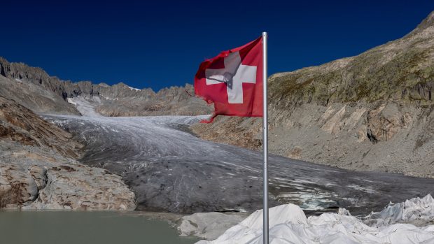 Švýcarská vlajka u vchodu do ledové jeskyně na ledovci Rhone (ilustrační foto)