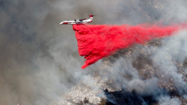 Hasiči letecky shazují růžovou směs vody, hnojiva a barvy