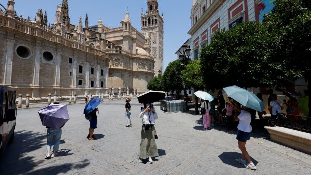 Turisté v Seville na jihu Španělska se chrání deštníky před sluncem