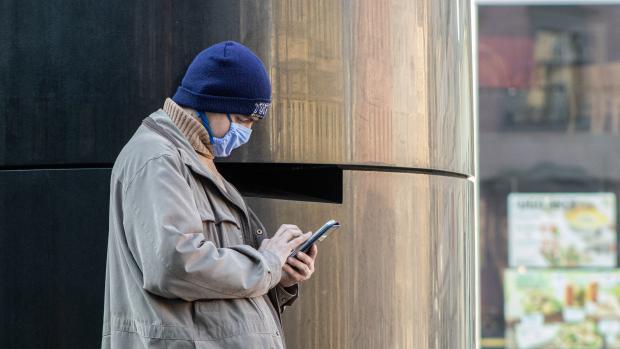 Muž se dívá do telefonu a opírá se o brněnský orloj na náměstí Svobody