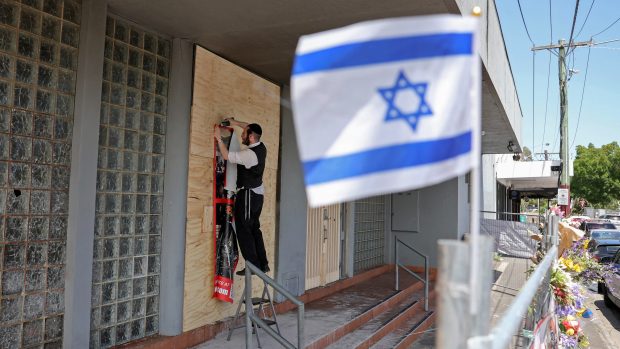 Člen židovské komunity připevňuje plakát na průčelí poškozené synagogy v Melbourne