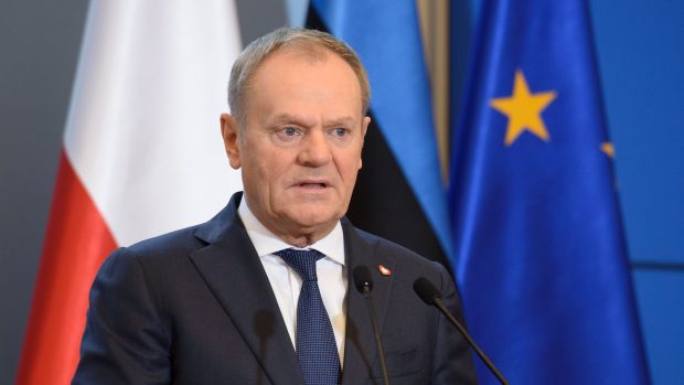 Polský premiér Donald Tusk s polskou, estonskou a unijní vlajkou v pozadí.