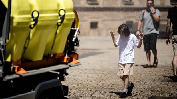 Děti se chladí v rozprašovači vody z pojízdné cisterny při kropení nádvoří Pražského hradu