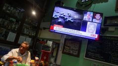 Barman stojí u televize, kde se vysílá zpráva o zatčení mexického drogového bosse Ismaela „El Mayo“ Zambady