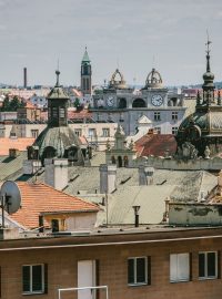 Plzeňské střechy s věží Mrakodrapu na Americké třídě uprostřed snímku. Střechu zdobí dvě nástavby s hodinami a dvě věže ve tvaru koruny, které vzdáleně připomínají střechy soudobých amerických mrakodrapů