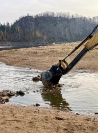 Bagr rozhrnuje cestičku na ostrov, kterou lidé postavili z kamenů