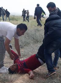 Muži odnášejí jednoho z desítek zraněných Palestinců. Těch na několika místech podél hraniční linie pásma Gazy s Izraelem protestuje na 17 000 lidí.