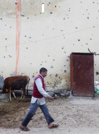 Muž prochází kolem prostřílené fasády domu ve vesnici na pákistánské straně hranice