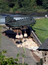 V pátek na pomoc dorazil také armádní vrtulník typu Chinook, který začal shazovat na poškozené místo pytle se směsí písku, štěrku a kamení