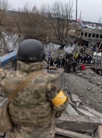 Ukrajinský voják a obyvatelé ukrajinského města Irpiň překračují zničený most, aby unikli před raketovým útokem