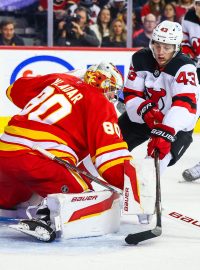 Brankář Calgary Flames Daniel Vladař zasahuje proti Lukeu Hughesovi z New Jersey Devils