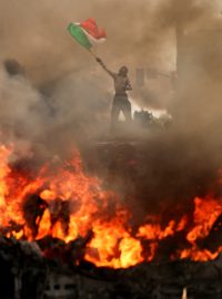 Zatímco protestující v Los Angeles mává mexickou vlajkou, před ním hoří vozidlo. Lidé demonstrují proti migrační politice administrativy Donalda Trumpa