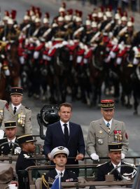 Francouzský prezident Emmanuel Macron stojí v velitelském voze s náčelníkem generálního štábu francouzských ozbrojených sil (CEMA) Thierrym Burkhardem během každoroční vojenské ceremonie k oslavě Dne dobytí Bastily na bulváru Champs-Elysées v Paříži, Francie, 14. července 2025