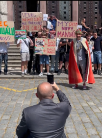 Šéf agentury Advertes fotí falešnou demonstraci. Několik účastníků drží bílý papír s QR kódem, který jim krátce předtím předal Leroy Weinrich a další pracovníci agentury